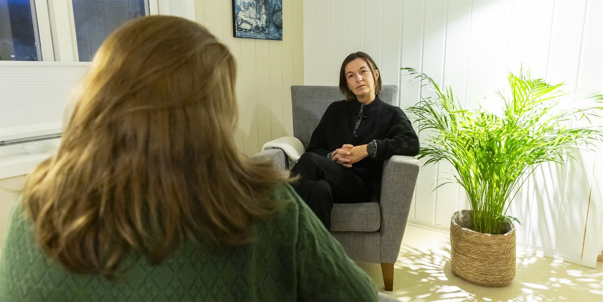 En kvinne med langt hår sitter med ryggen til og ser på Lisbeth, som sitter en stol på kontoret sitt.