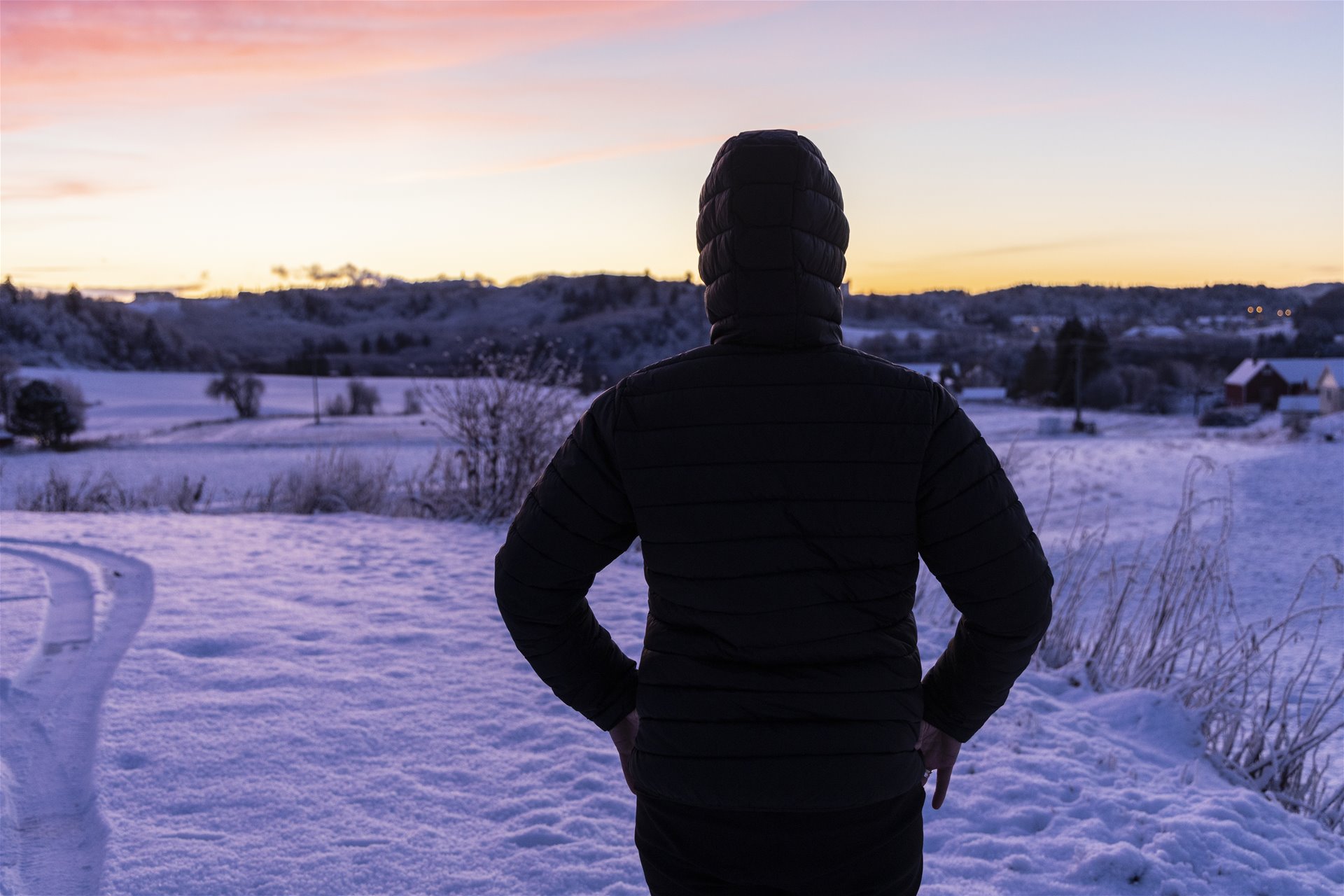 Åse med ryggen til, ser utover et snødekt landskap mot solnedgangen