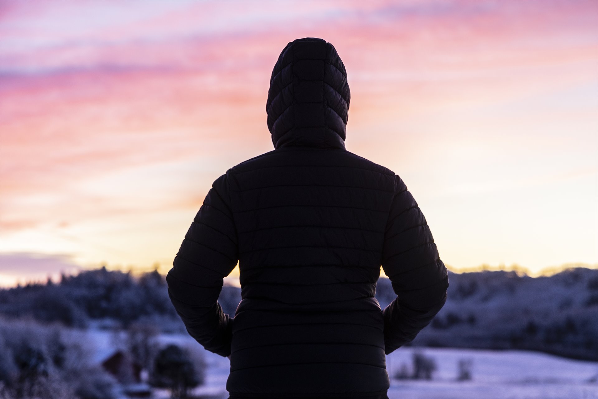 En mørk skikkelse ser på solnedgangen bak et snødekt landskap.